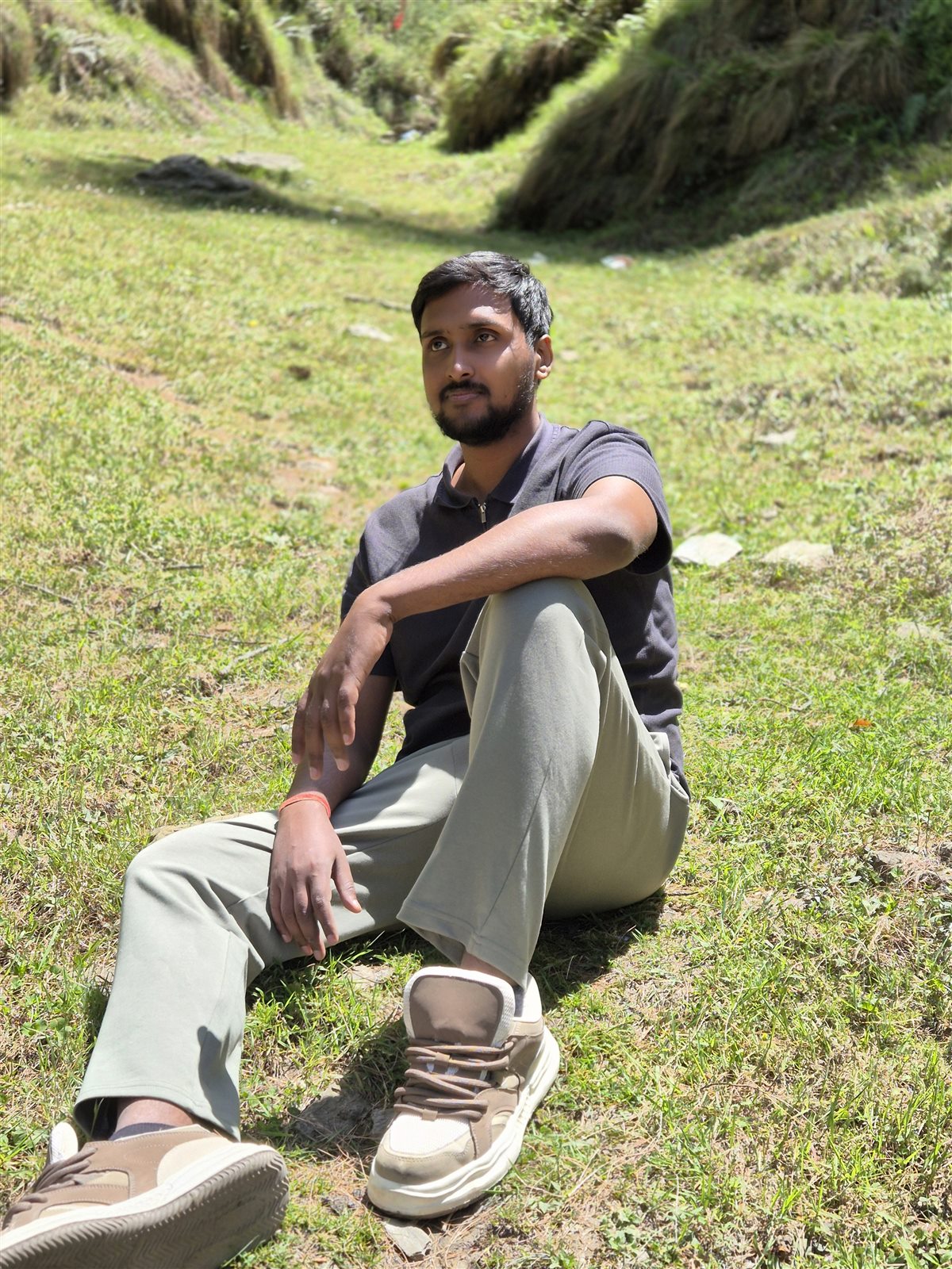 Vishwas Jha sitting on a grassy hillside during a mountain trek
